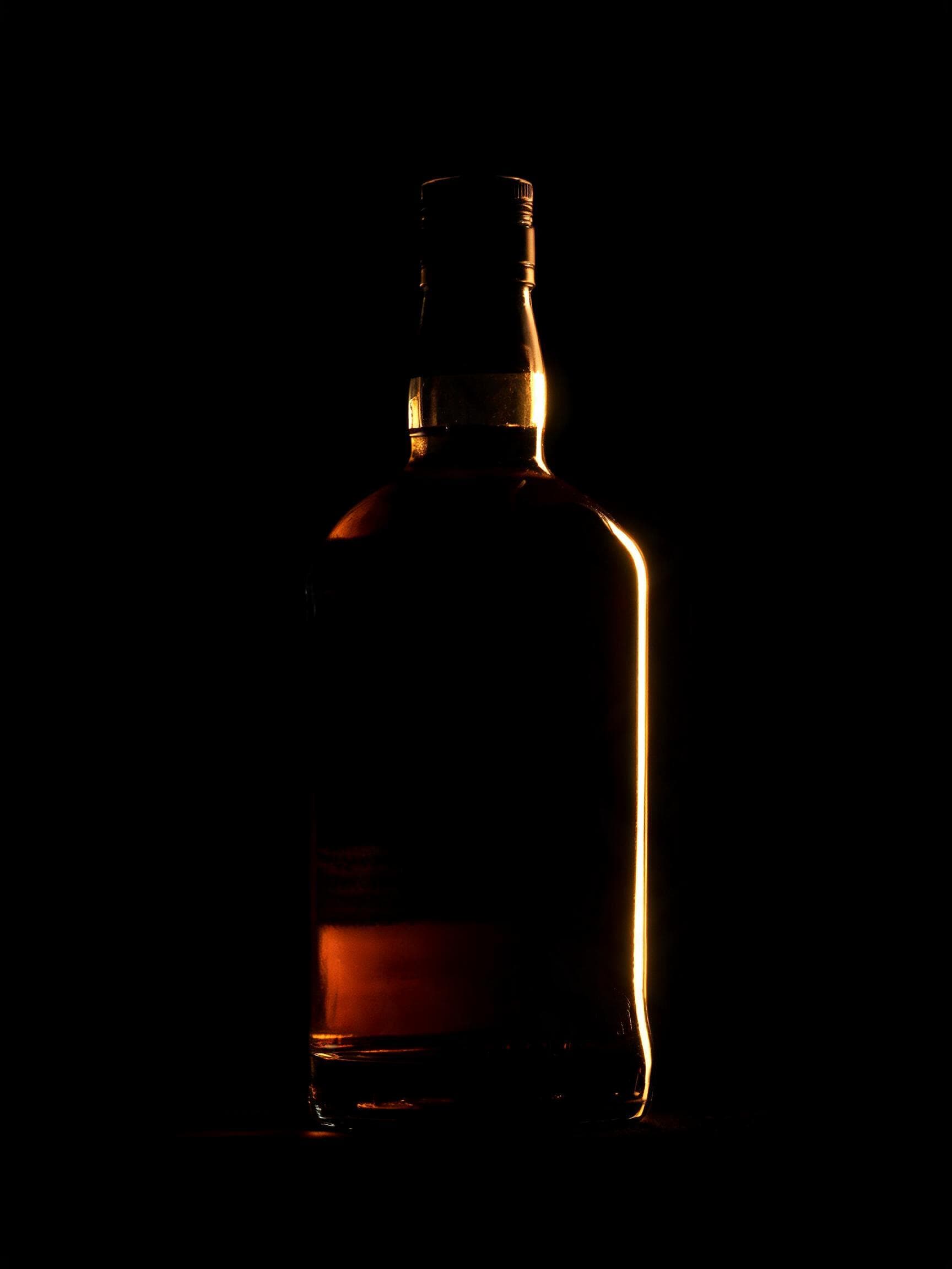 A dark spirit bottle silhouetted against warm backlight